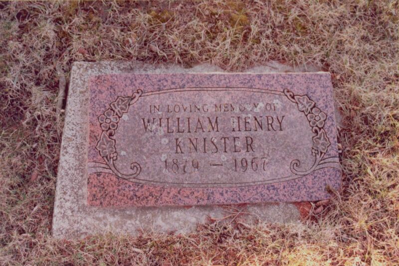 Photo of a flat pink gravestone inlaid in the ground surrounded by brown grass. 