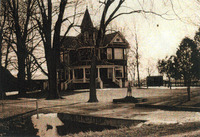 Sepia tinted photo of a large house with trees lining its lawn. There's a statue of a dog on the lawn, and a concrete driveway. 