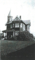 Black and white image of a large home in with a neatly cut lawn. There are two children visible on the steps. 