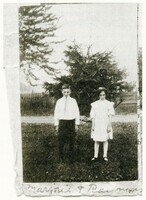Black and white photo of Raymond and Marjorie Knister as children looking directly at the camera. Raymond is standing on the left in a white shirt and black pants, and Marjorie is on the right in a white dress. 