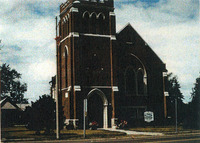 A photo of a brick church with a rectangular tower on the left side of the building, and a shorter right side, with an inverted triangular roof. 